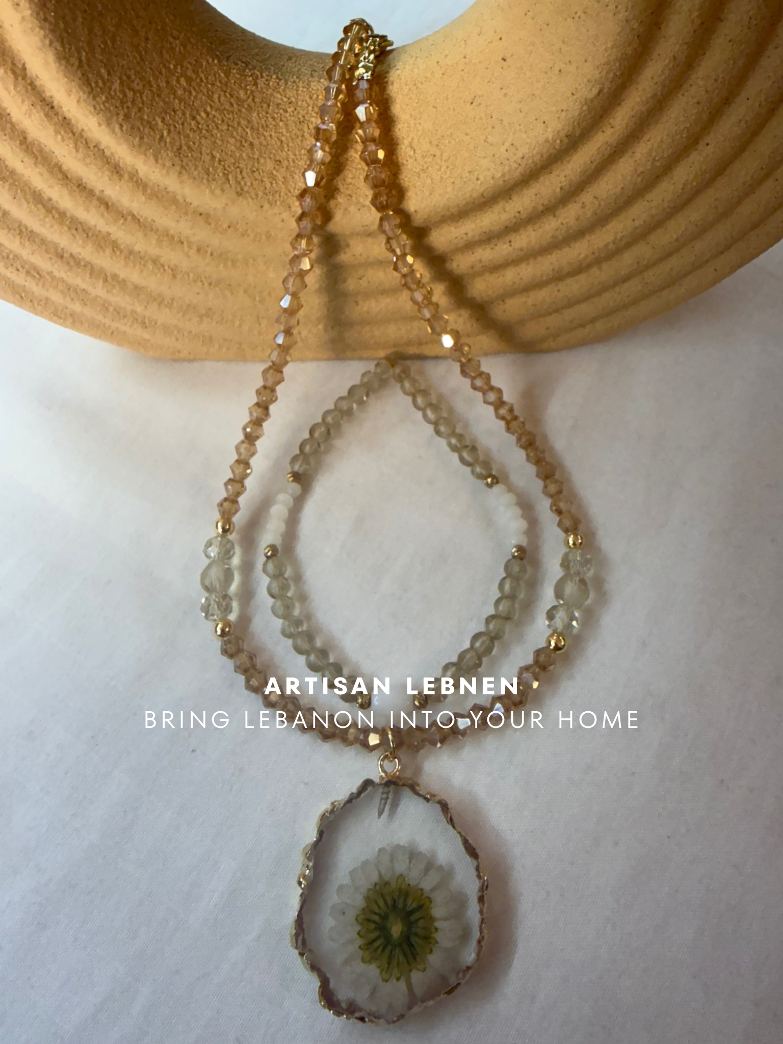 Necklace with a floral pendant on a textured surface, featuring the brand 'Artisan Lebnen'.