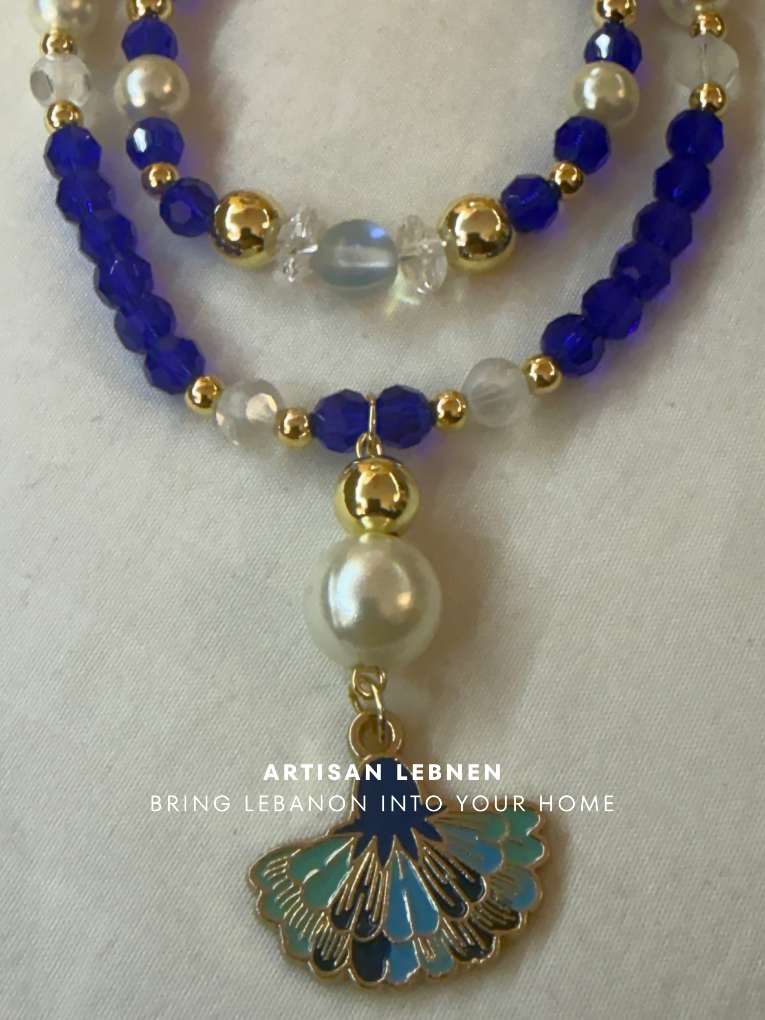 Beaded necklace with a shell pendant on a white background, featuring the brand 'Artisan Lebanon'.