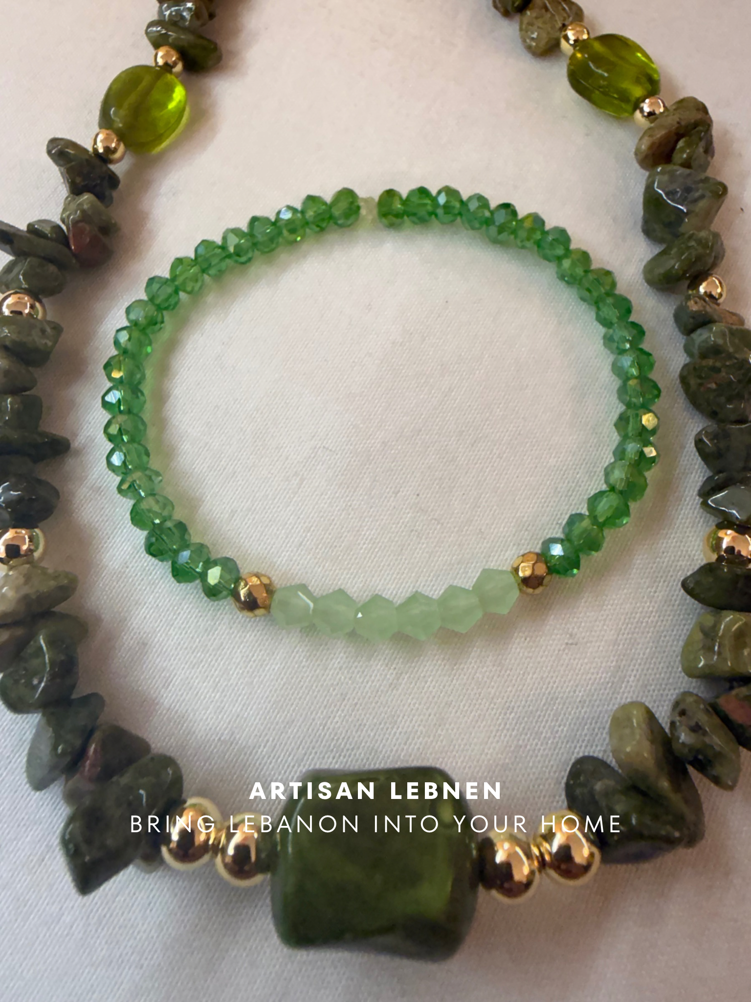 Green beaded bracelet with gold accents on a white fabric background, featuring the brand 'Artisan Lebnen'.