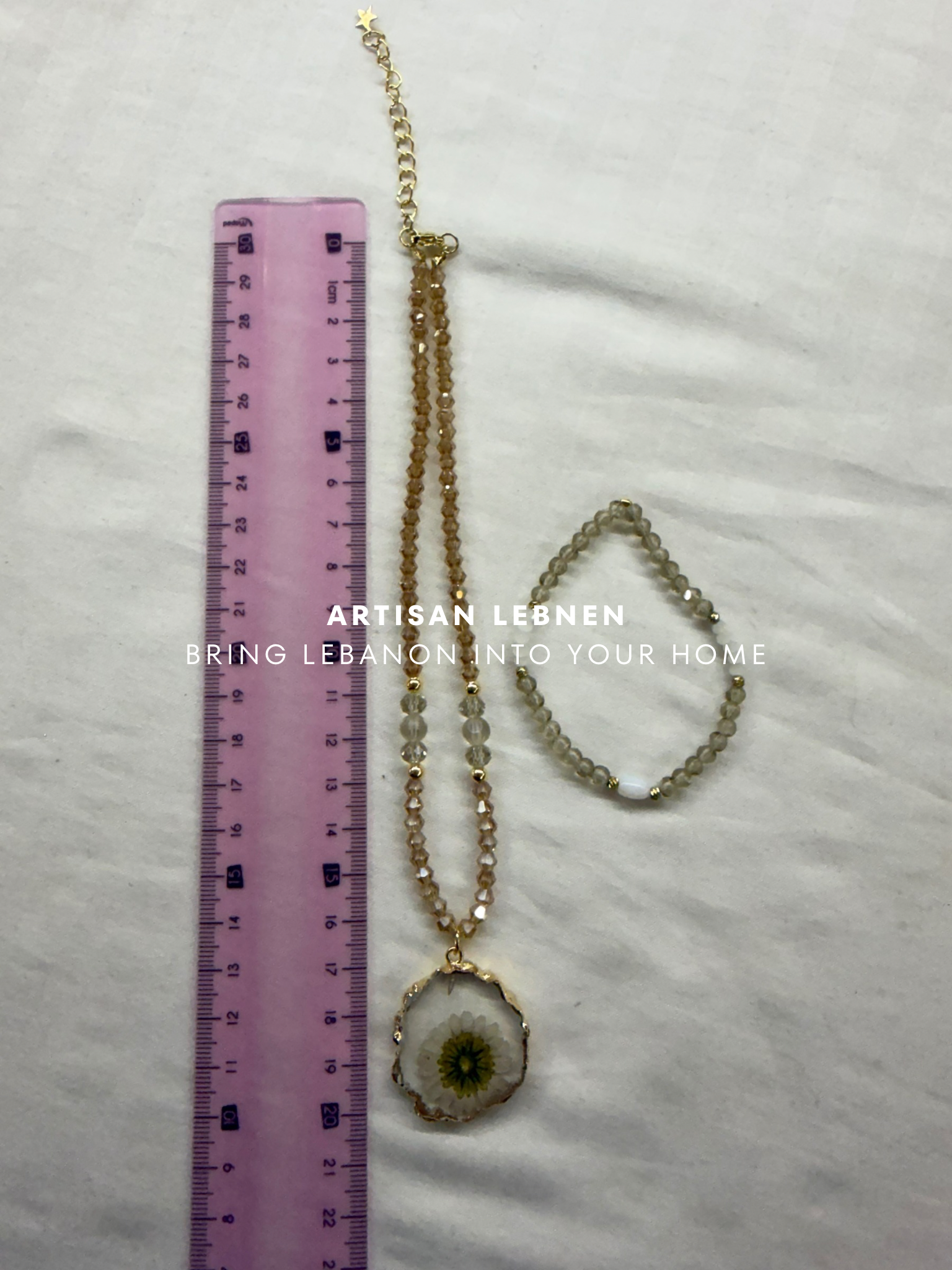 Necklace with pendant and bracelet next to a ruler on a white surface, with 'Artisan Lebnen' branding.