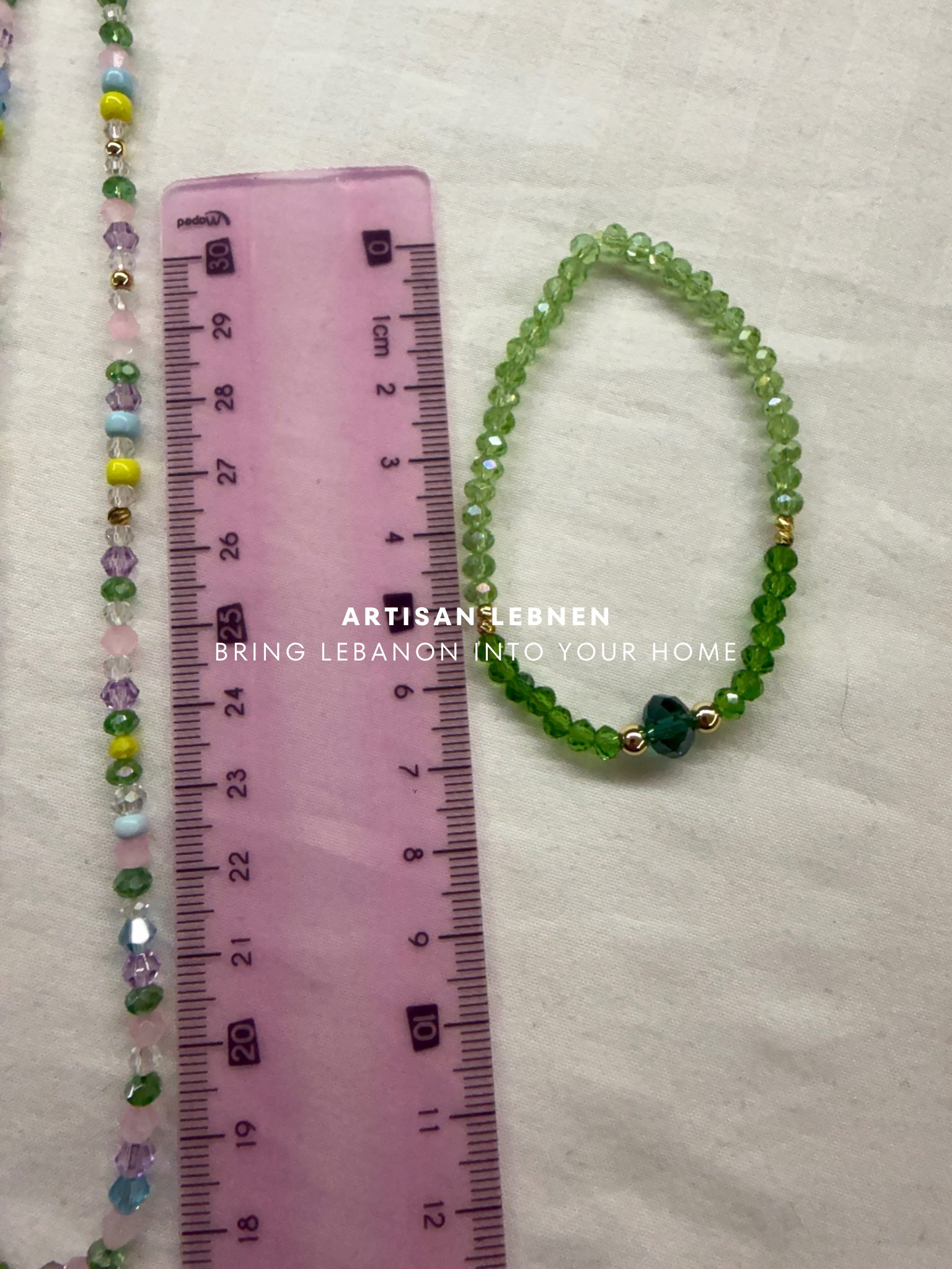 Green beaded bracelet next to a ruler on a white background with 'Artisan Lebnen' branding.
