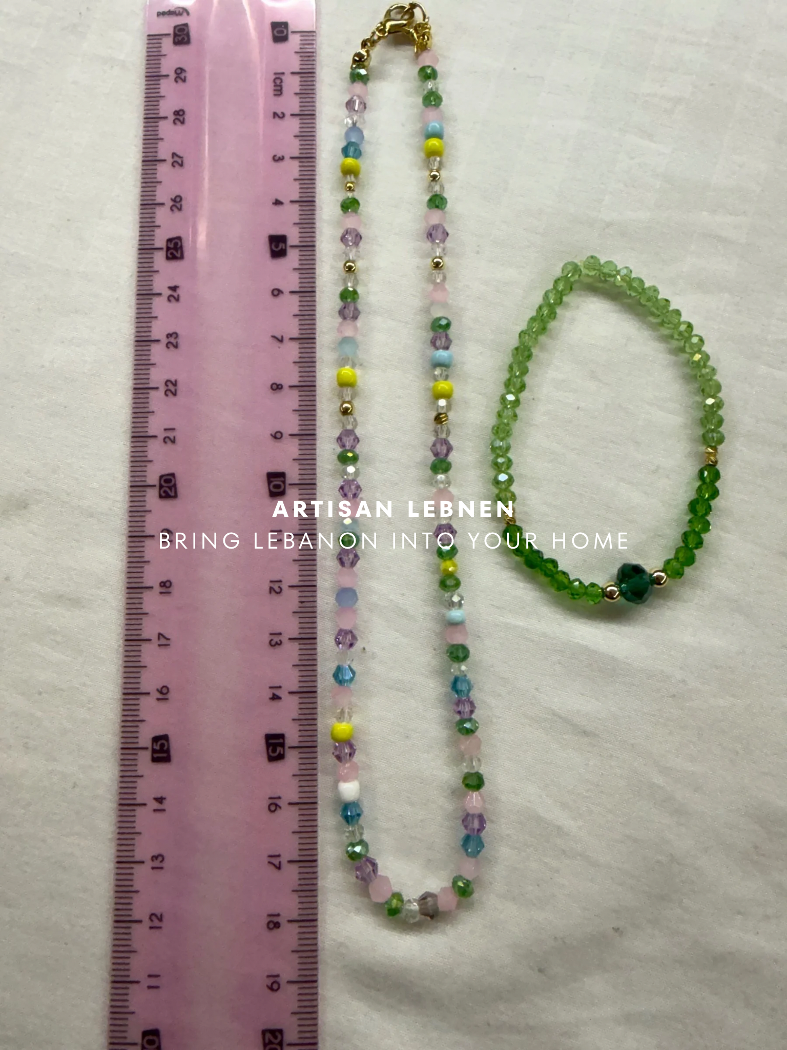 Beaded necklace and bracelet with a ruler for scale on a textured surface, featuring 'Artisan Lebnen ' branding.