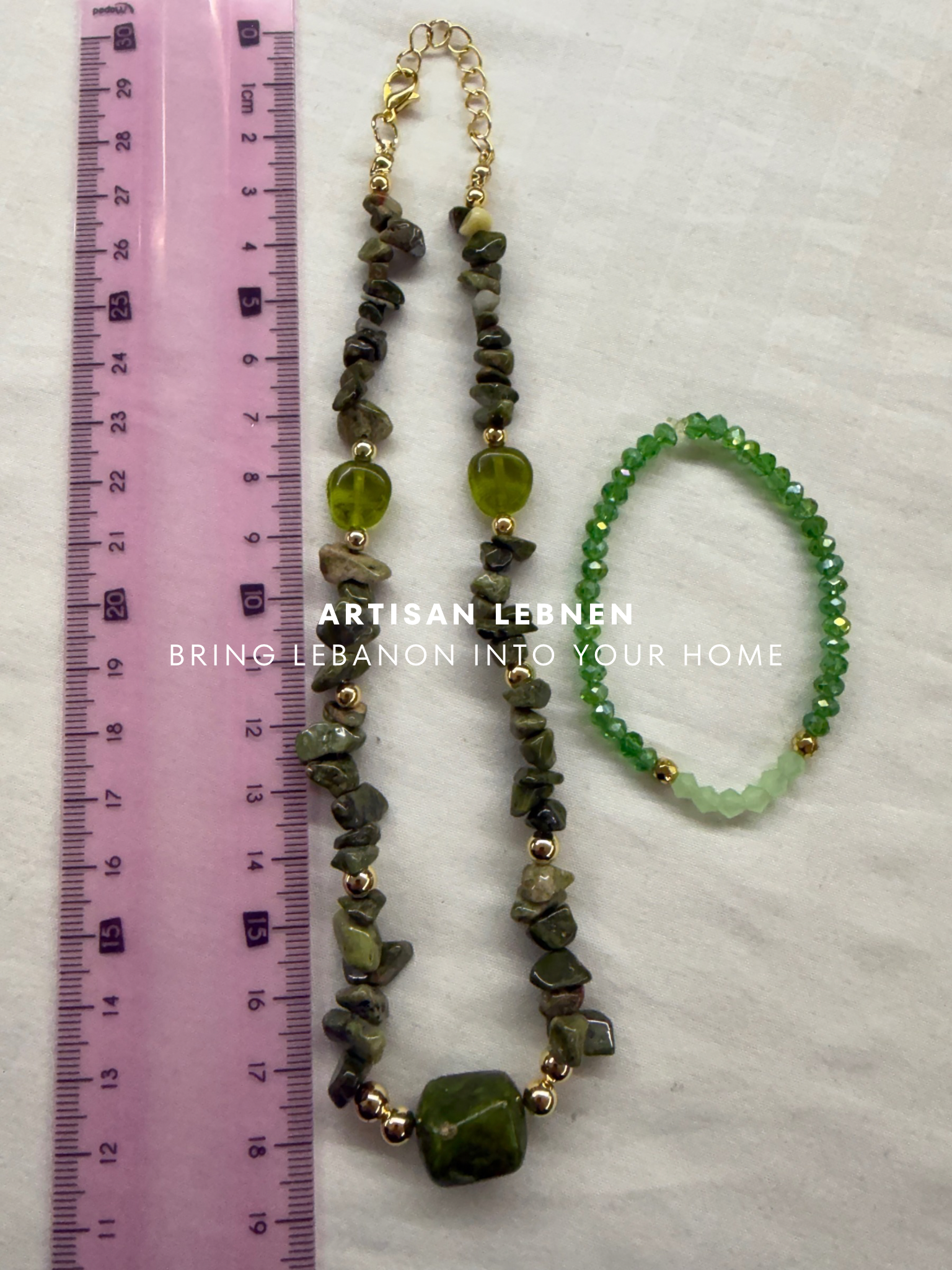 Green beaded necklace and bracelet with gold accents on a white background, next to a pink ruler.