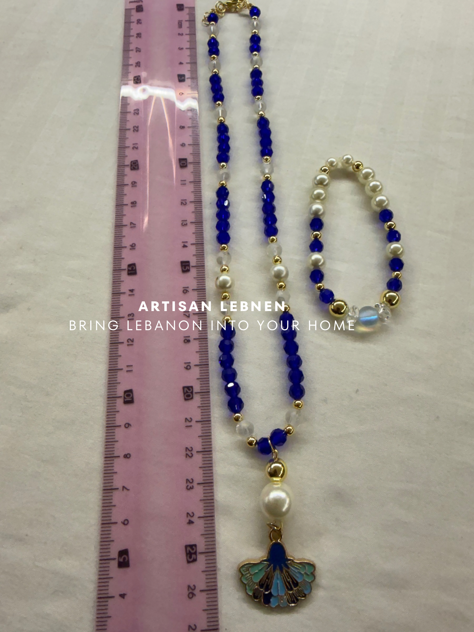 Necklace with blue beads and a butterfly pendant next to a ruler on a light background