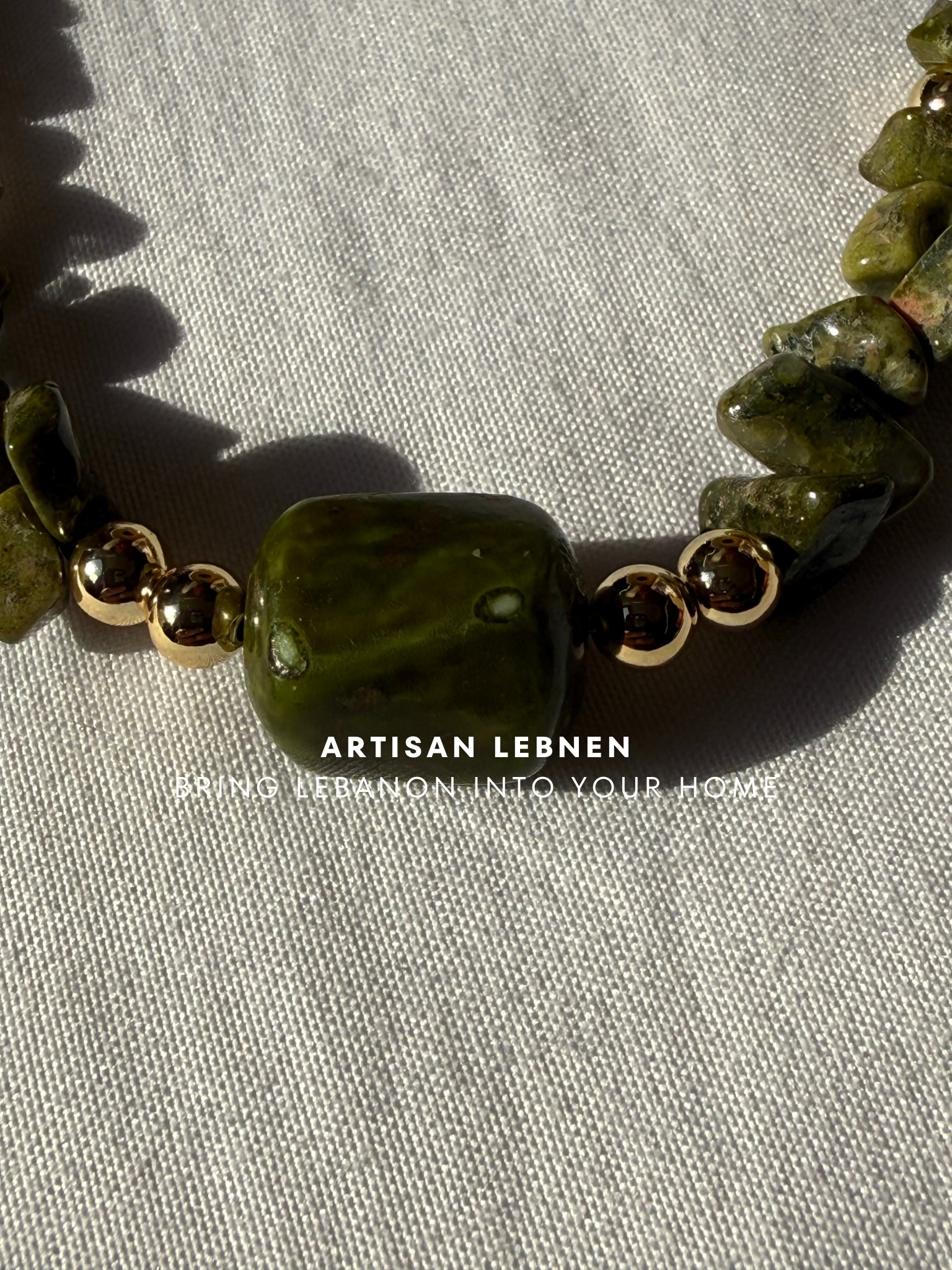 Necklace with green beads on a textured surface, featuring the brand 'Artisan Lebnen '.