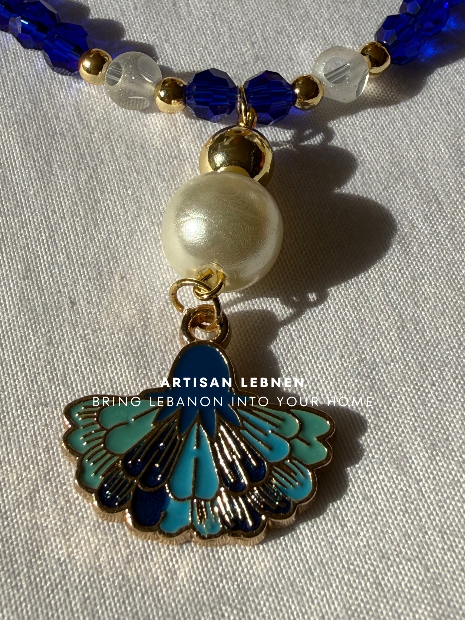 Necklace with blue, white, and gold beads and a decorative pendant on a light gray background.