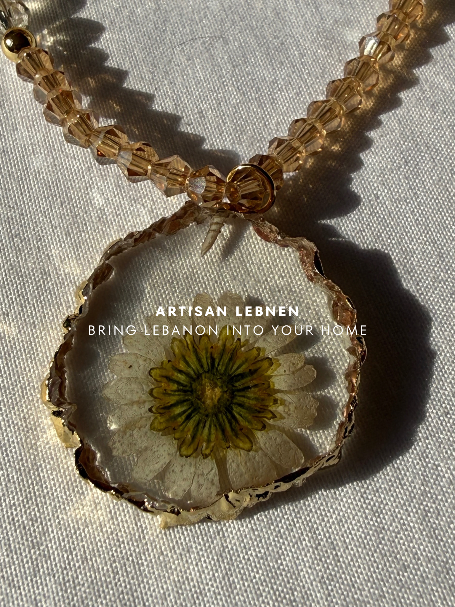 Necklace with a pendant featuring a pressed flower, on a light fabric background.